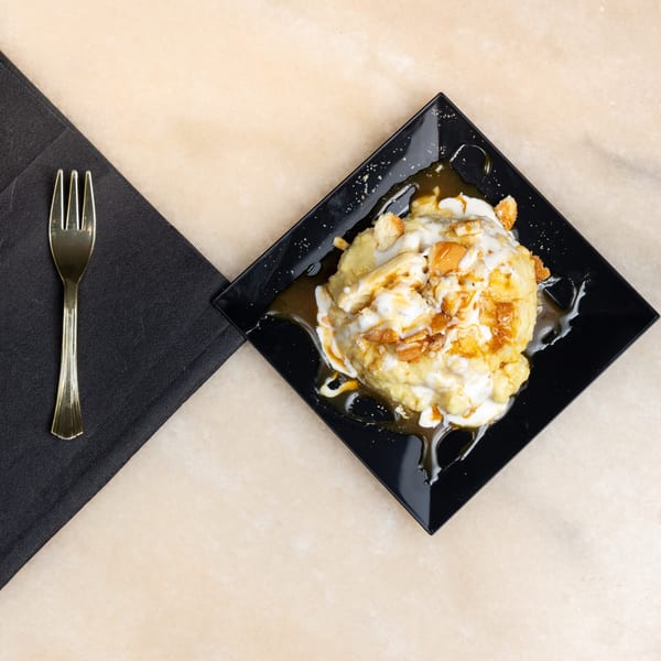 Banana pudding dessert with whipped cream, caramel, and cookie crumbles on a black plate.
