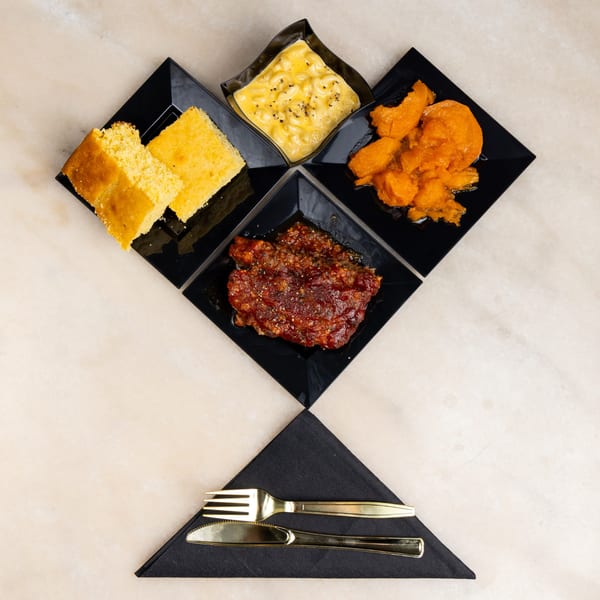 Four black square dishes arranged in a diamond shape, holding cornbread, mac and cheese, candied yams, and meatloaf.