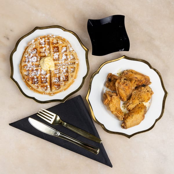 Golden waffle with butter and powdered sugar, fried chicken wings, and black syrup dish on a marble surface.