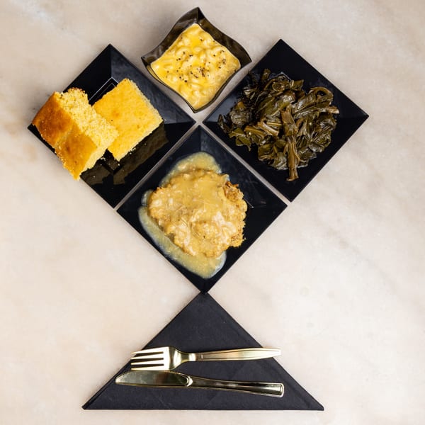 Top-down view of a soul food meal with cornbread, mac and cheese, collard greens, and smothered chicken.