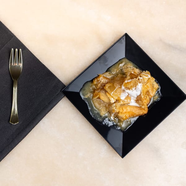 Golden apple cobbler with vanilla ice cream and sauce on a black plate with a fork.