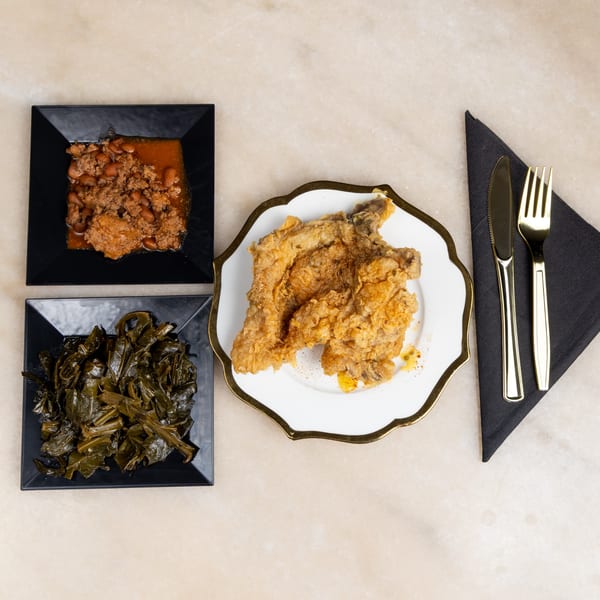 Fried chicken, collard greens, and baked beans with ground meat on a light-colored surface.